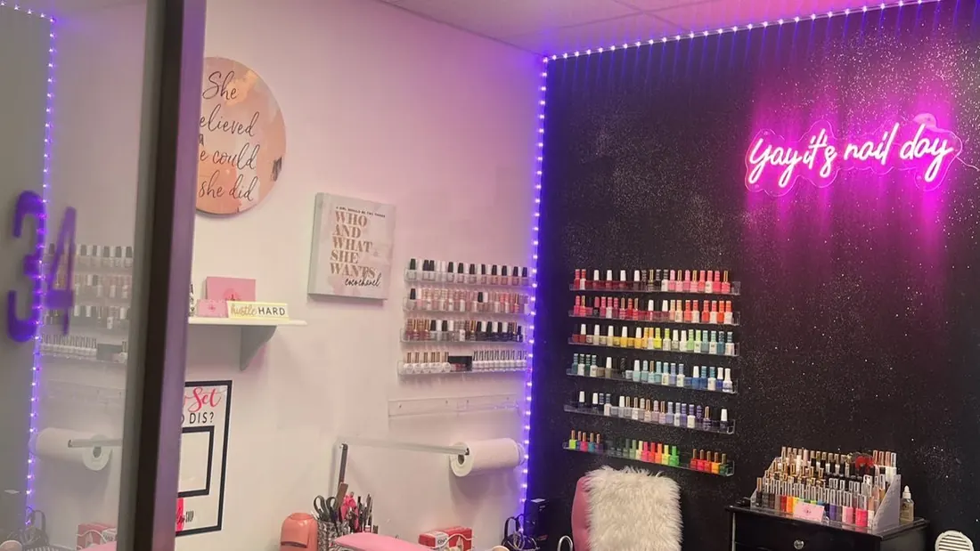 Nail studio with a glitter accent wall, neon sign and rows of gel polish